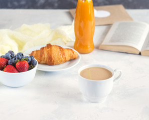 Breakfast with croissant, berries and book on white background