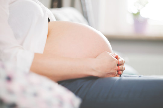Belly of pregnant woman sitting on sofa at home