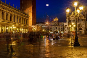 Fototapeta na wymiar Piazza San Marco, Venice, Italy, illuminated at night with lots of unrecognizable people, colorful sky, stars and full moon