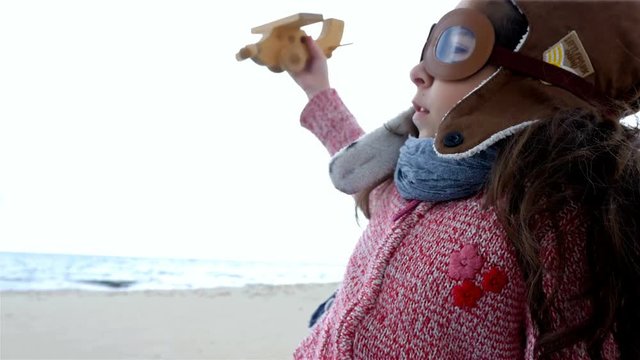 Little girl with pilot hat playing with wooden airplane against blue sky
