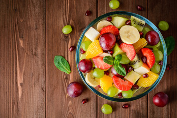 Healthy fresh fruit salad in glass bowl on wooden background.