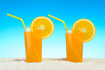Two glasses of orange juice on the beach