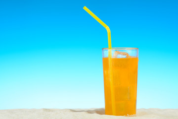 A glass of orange juice with ice on the beach