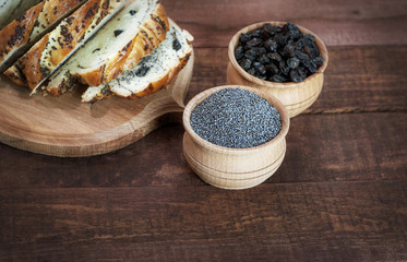 Poppy seeds and raisins in wooden bowls on a brown surface