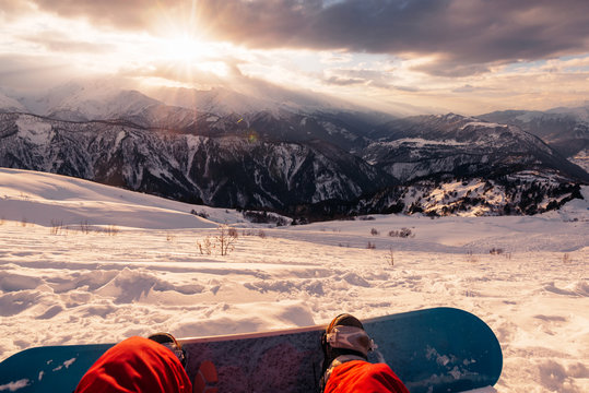 snowboarder with snowboard is sitting on the mountain on the sunset