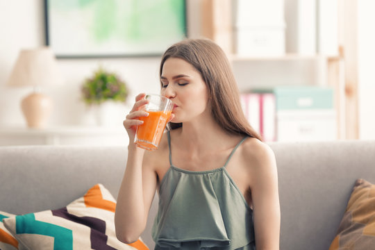 Young woman tasting fresh juice sitting on couch at living room