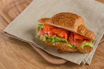 Croissant sandwich with fish salmon. Homemade fast food recipe dishes. Top view, overhead. Rustic background.