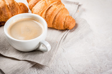 Continental traditional breakfast. Croissant, a cup of coffee. On a white stone concrete table. Copy space