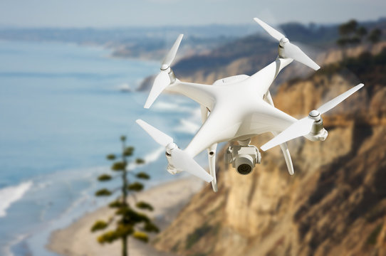 Unmanned Aircraft System (UAV) Quadcopter Drone In The Air Over The Ocean Coastline.