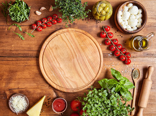 Cutting wooden board with traditional pizza preparation ingridients: mozzarella, tomatoes sauce,...