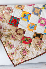 Part of color patchwork quilt with vintage flowers pattern lying on a white sofa as background. Colorful Scrappy blanket. Hobby concept.