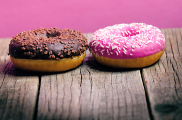 Donut with sprinkles on a wooden table and pink background. Two types of donuts. Cake and sweet. Food detail. Close up. Pastel color