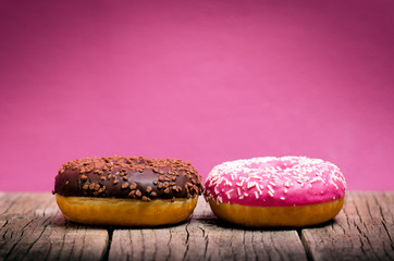 Donut with sprinkles on a wooden table and pink background. Two types of donuts. Cake and sweet. Food detail. Close up. Pastel color