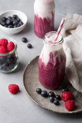 Healthy berry smoothie with yogurt in bottle on light concrete background