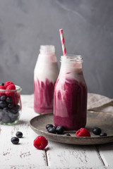 Healthy berry smoothie with yogurt in bottle on light concrete background