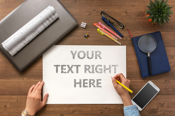 The girl sits at the table with a mobile phone, a laptop, business accessories and a sheet with text Your text