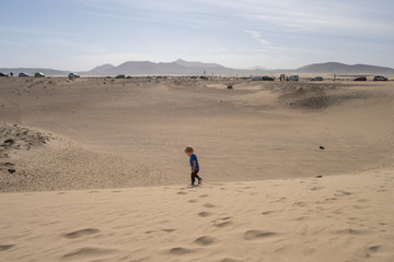 Fototapeta na wymiar Little boy is walking in the sand dunes 