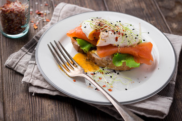 Delicious toast with salad, salted salmon and poached egg on rustic background