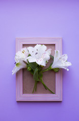 Empty photo frame with bouquet of white Alstroemeria on lilac background