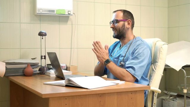 Happy male doctor finishing working on laptop and stretching arms in office
