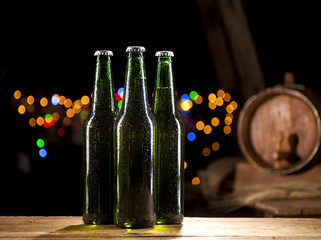 Glass bottles of beer and wooden barrel on bar lights background