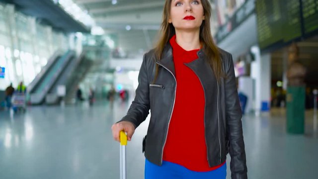 Woman in bright clothes is rolling yellow suitcase in the airport