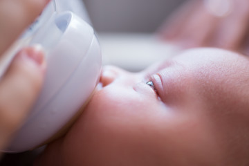 Close up of two week old newborn girl bottle fed by her mother. 