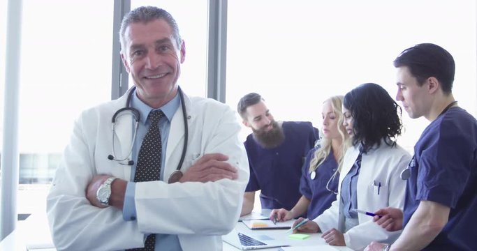 Confident relaxed doctor at hospital with team of doctors in background