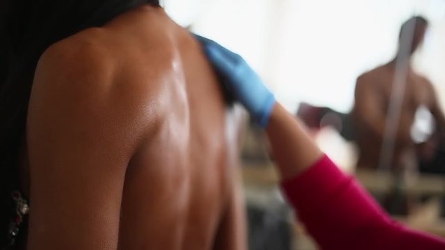 Applying body oil on female bodybuilder back. Getting ready for bodybuilding championship.