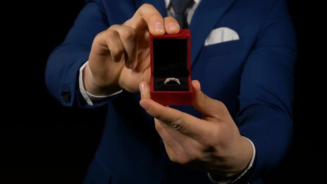 Close up with hands of business man opening small gift box with ring inside