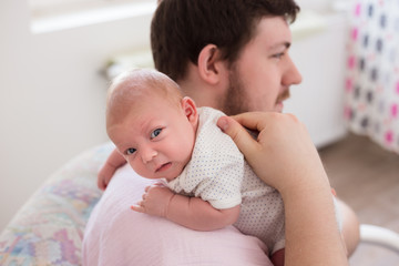 Young father burping his newborn daughter, holding her affectionately. 