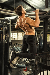 Fototapeta na wymiar Muscular man doing pull ups on bars at the gym