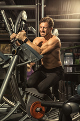 Fototapeta na wymiar Shirtless male athlete exercising on ab coaster gym machine