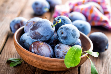 Fresh plums with green leaves on wooden rustic background