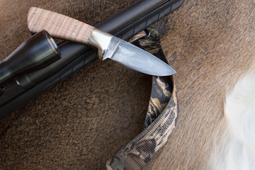 A fixed blade hunting knife sits atop a rifle on a deer hide