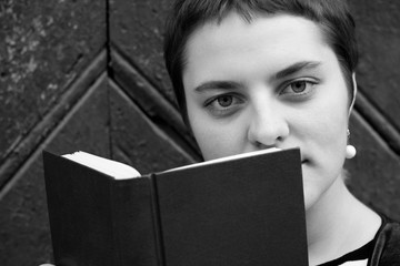 A girl with big eyes and short hair hides behind a book. Close-up portrait. Black and white photo