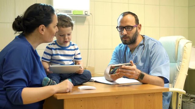 Doctor with smartphone talking to mother with child about test results in office
