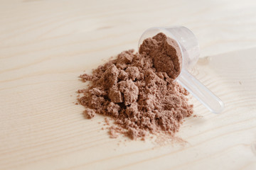 Product photograph of spoon or measuring scoop of whey protein on wooden background