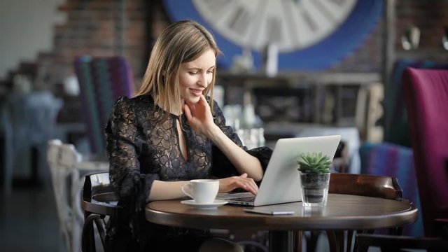 Beautiful woman in a cafe working with a laptop. A cheerful, happy girl, prints on the laptop's keyboard, she received good news, and shares them via social media.