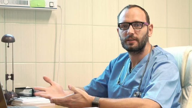 Unhappy male doctor talking bad news sitting by table in office
