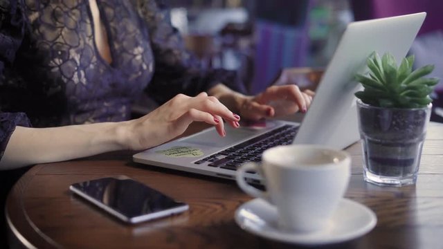 Beautiful woman in a cafe working with a laptop. A cheerful, happy girl, prints on the laptop's keyboard, she received good news, and shares them via social media.