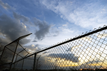Empty community baseball diamond and fence in silhouette against a sunset sky at dusk