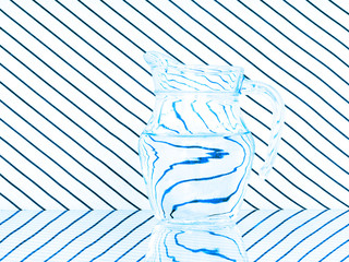 Glass jug on striped background. Reflection and refraction. - obrazy, fototapety, plakaty