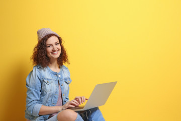 Beautiful young woman using laptop on color background