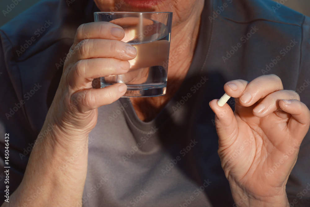 Poster Elderly woman taking pill at home, closeup