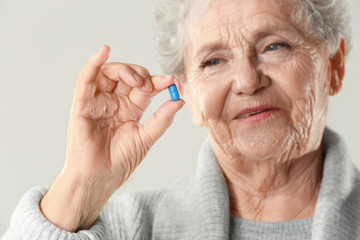 Elderly woman with pill on light background, closeup