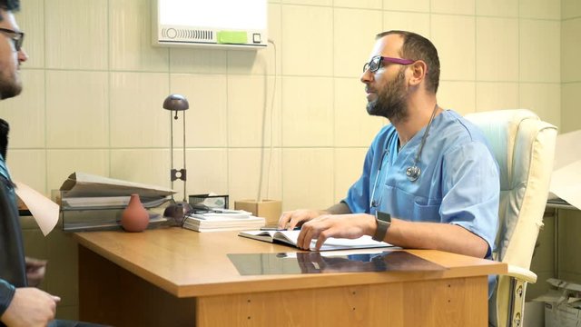 Male doctor and his patient talking in office in hospital
