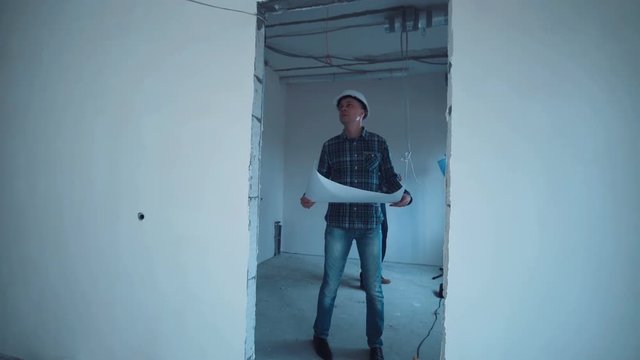 A taskmaster walking on a construction site with the plan then he stop and looking on camera and smile