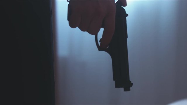 RL DOLLY Silhouette of male criminal pulling back the hammer of a pistol near the window. 4K UHD RAW edited footage