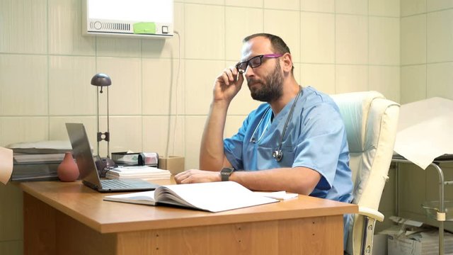 Tired male doctor yawning and falling asleep by table in office
